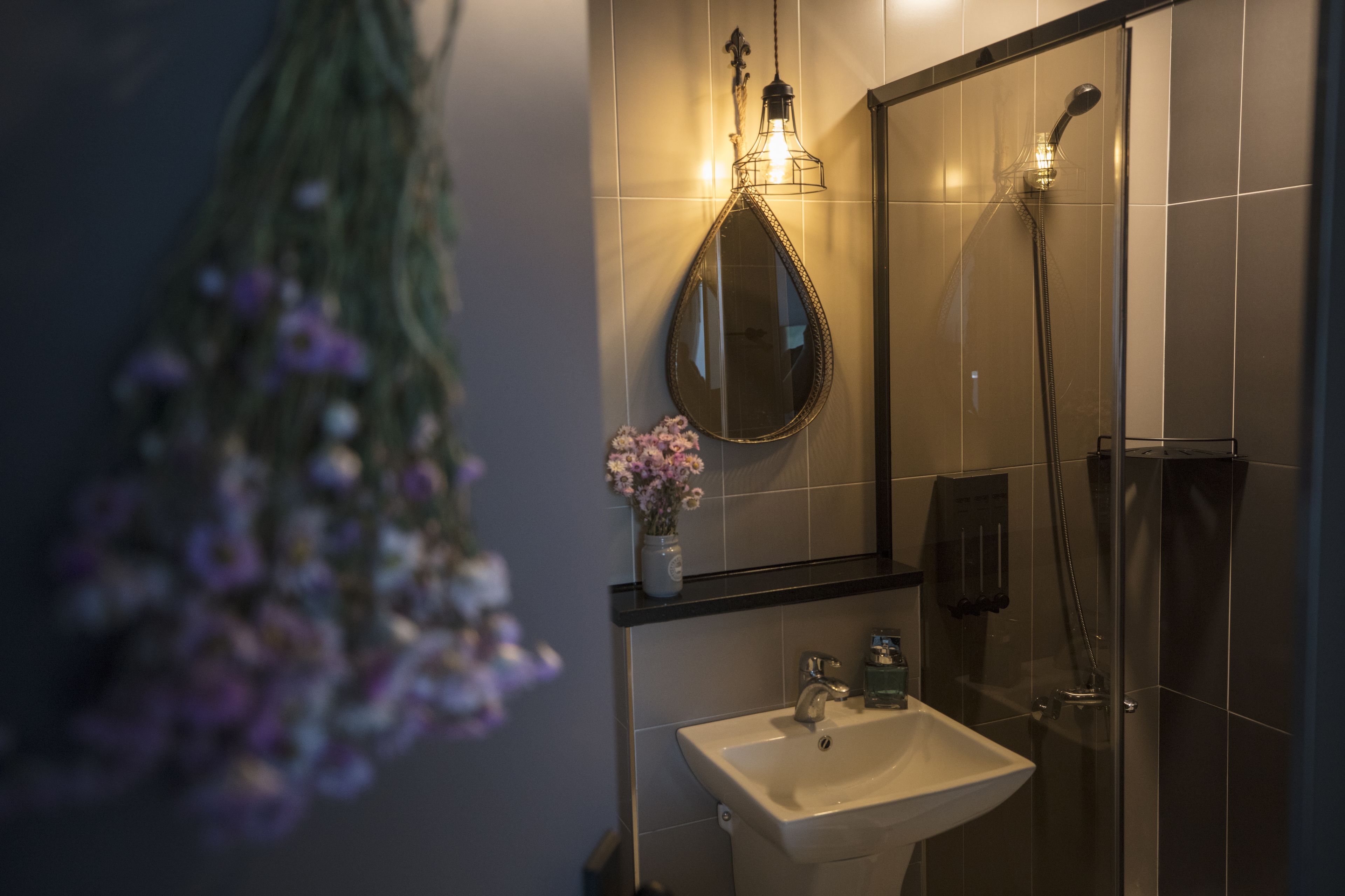 A bathroom with a sink, mirror, shower, and decorative flowers.