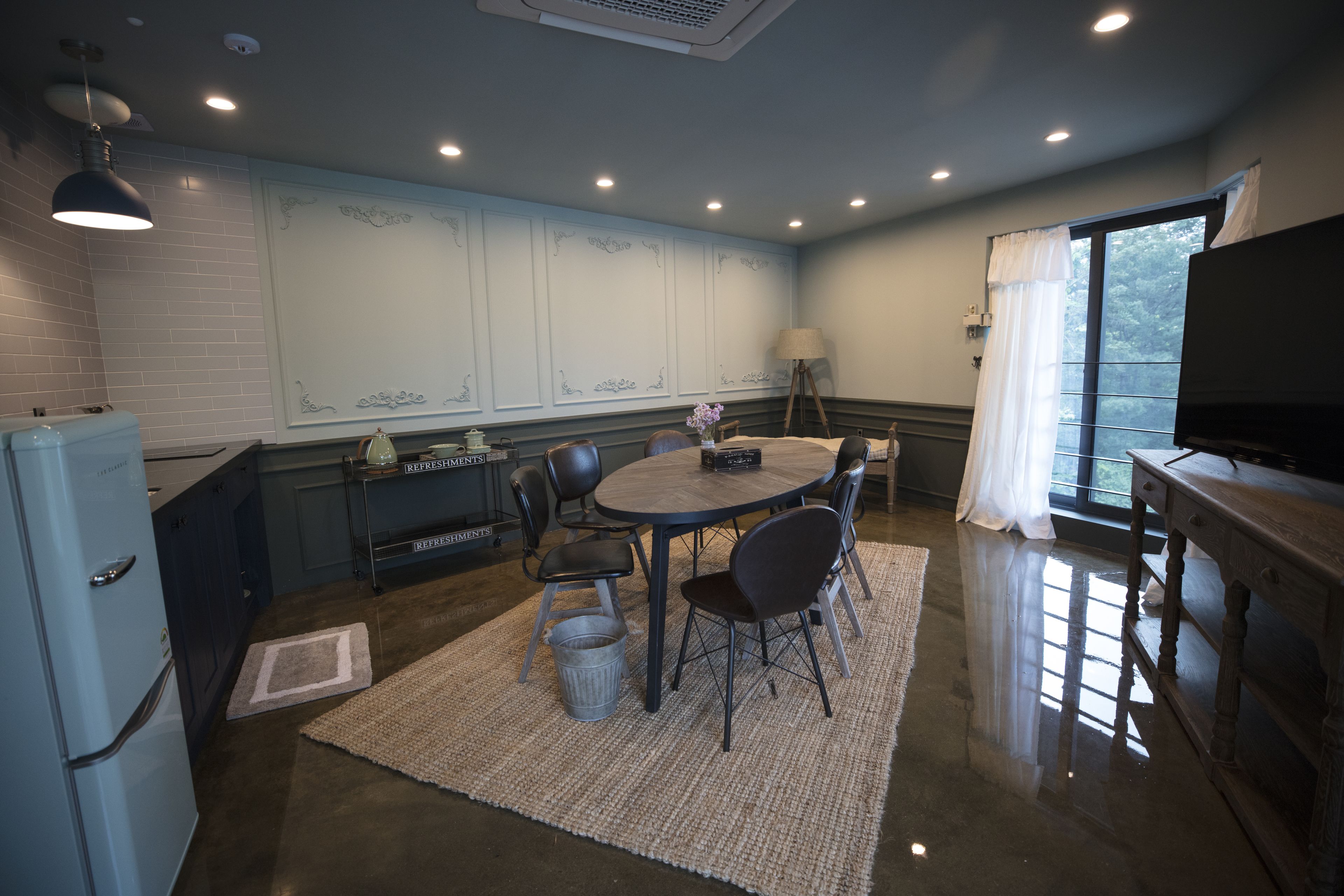 A compact kitchen with a dining area, a refrigerator, a table with chairs, and a television on a wooden cabinet.