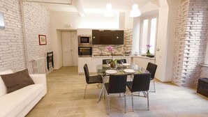 A modern kitchen with a dining area, white brick walls, and a white sofa. - Take Me Rome - Modern Apartment near Colosseum (Roma)