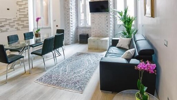A modern living room with a glass dining table, black sofa, and a small round table with a green plant. - Take Me Rome - Modern Apartment near Colosseum (Roma)