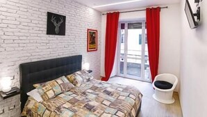 A bedroom with a bed, a white brick wall, a red curtain, and a white chair. - Take Me Rome - Modern Apartment near Colosseum (Roma)