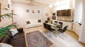 A modern apartment with a white brick wall, a dining area with a glass table and chairs, a white sofa, and a kitchen with a large window. - Take Me Rome - Modern Apartment near Colosseum (Roma)