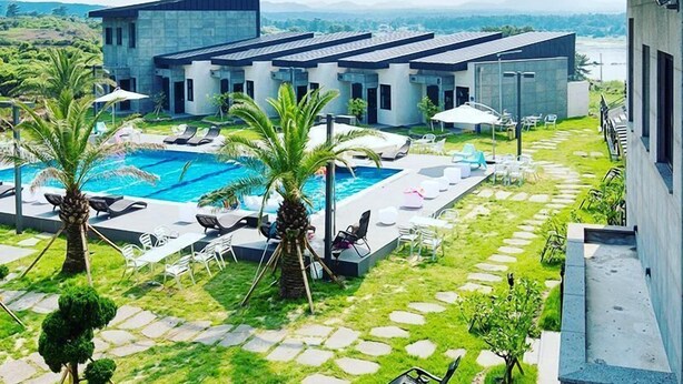 A modern hotel with a swimming pool, palm trees, and a view of the mountains. - Christmas Resort (Jeju City)