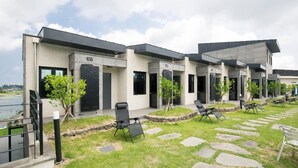 A modern building with numbered units 106 and 105, outdoor seating, and a stone pathway. - Christmas Resort (Jeju City)