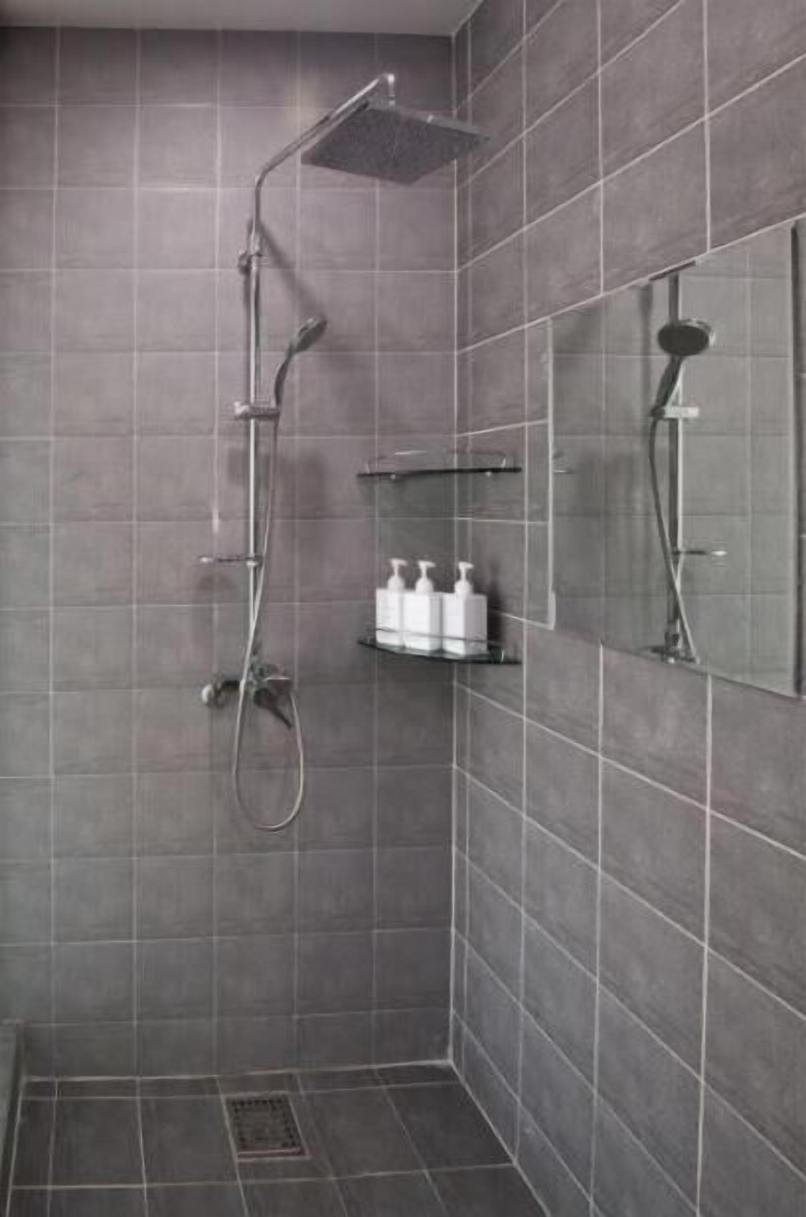 A modern shower area with a handheld showerhead, a wall-mounted faucet, and a shelf with toiletries.