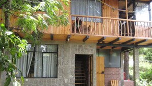 A rustic wooden house with a stone facade, a balcony with a wooden railing, and a brick wall. - Tzikin Jaay (San Pedro La Laguna)