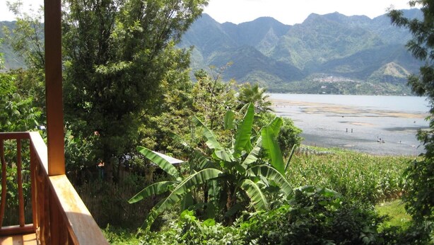 A view from a wooden deck overlooking a lake with mountains in the background. - Tzikin Jaay (San Pedro La Laguna)