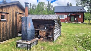 Un rustico chalet in legno con un camino, una struttura in tronchi e una casa rossa sullo sfondo.