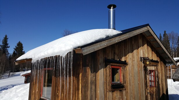 Una baita di legno con tetto imbiancato dalla neve e stalattiti che pendono dai cornicioni.