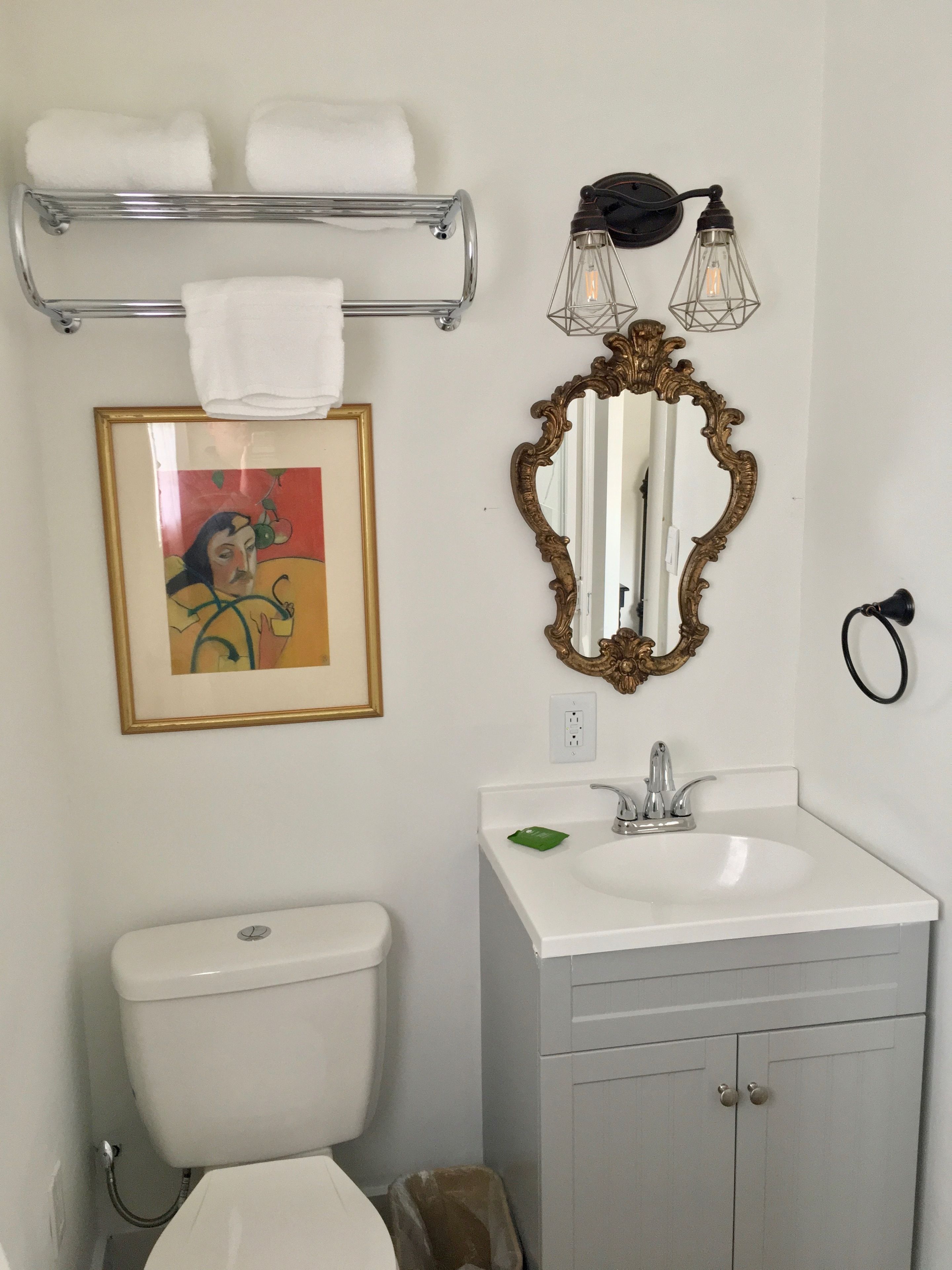Een badkamer met toilet, wastafel, spiegel, handdoekhouder en een lijst met een afbeelding aan de muur.