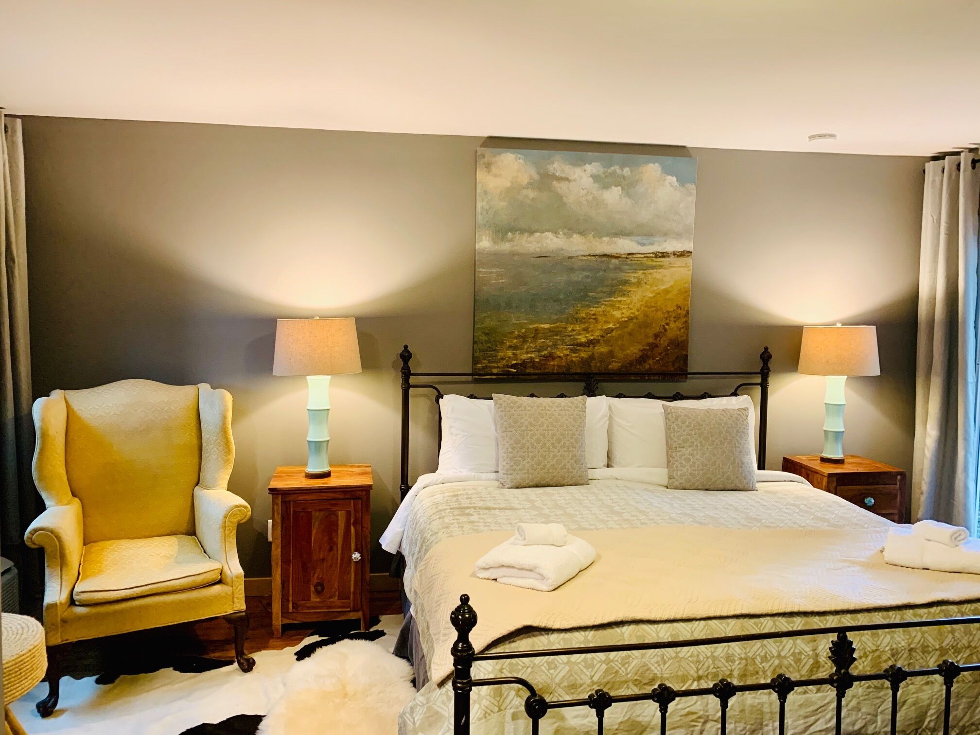 A bedroom with a bed, two bedside tables with lamps, a chair, a painting on the wall, and a rug.
