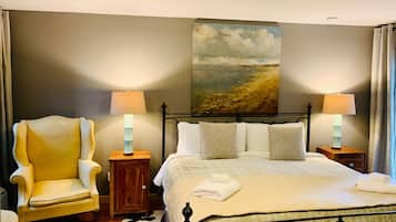 A bedroom with a bed, two bedside tables with lamps, a chair, a painting on the wall, and a rug.