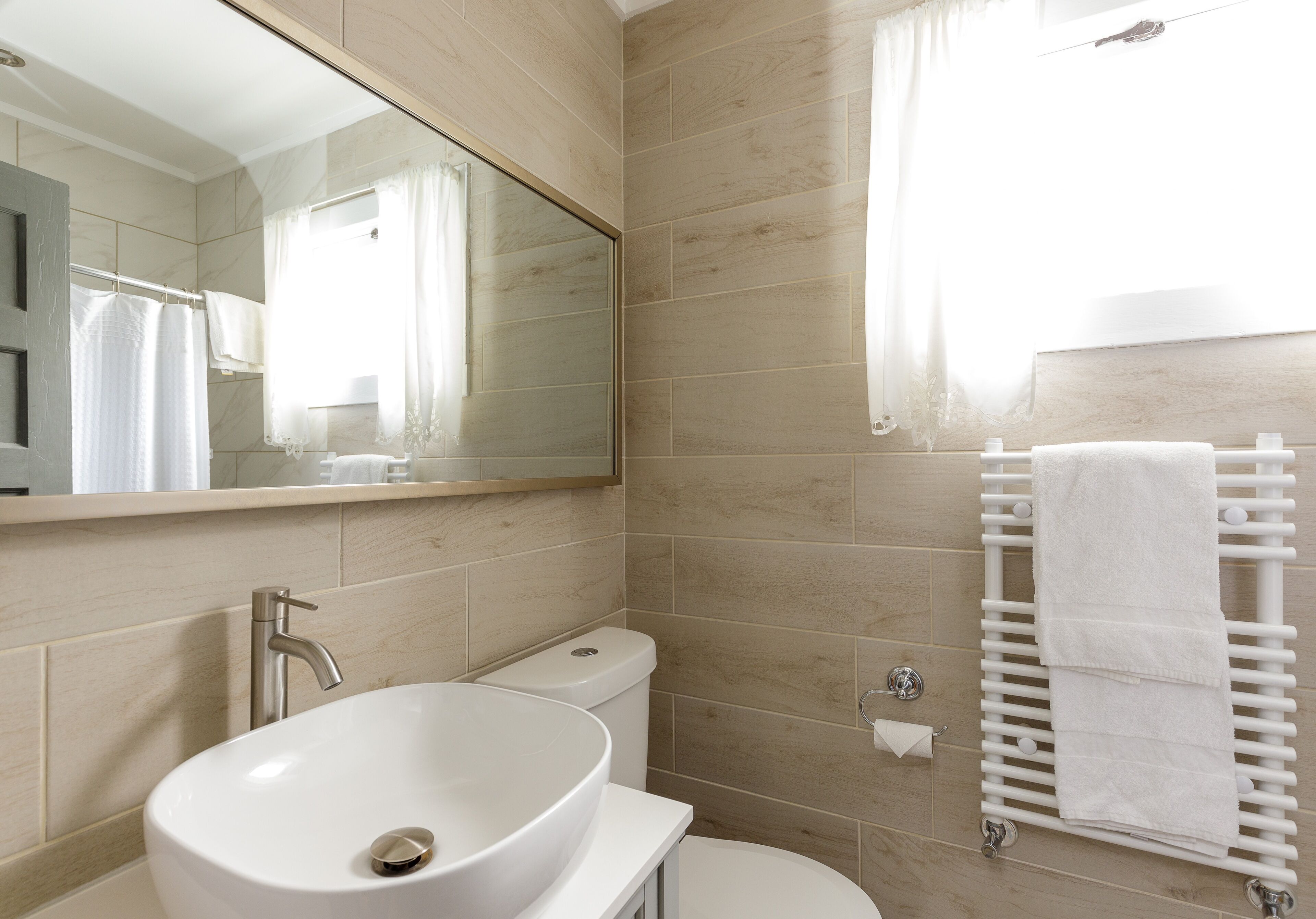 A modern bathroom with a large mirror, a white sink, a toilet, and a towel rack.