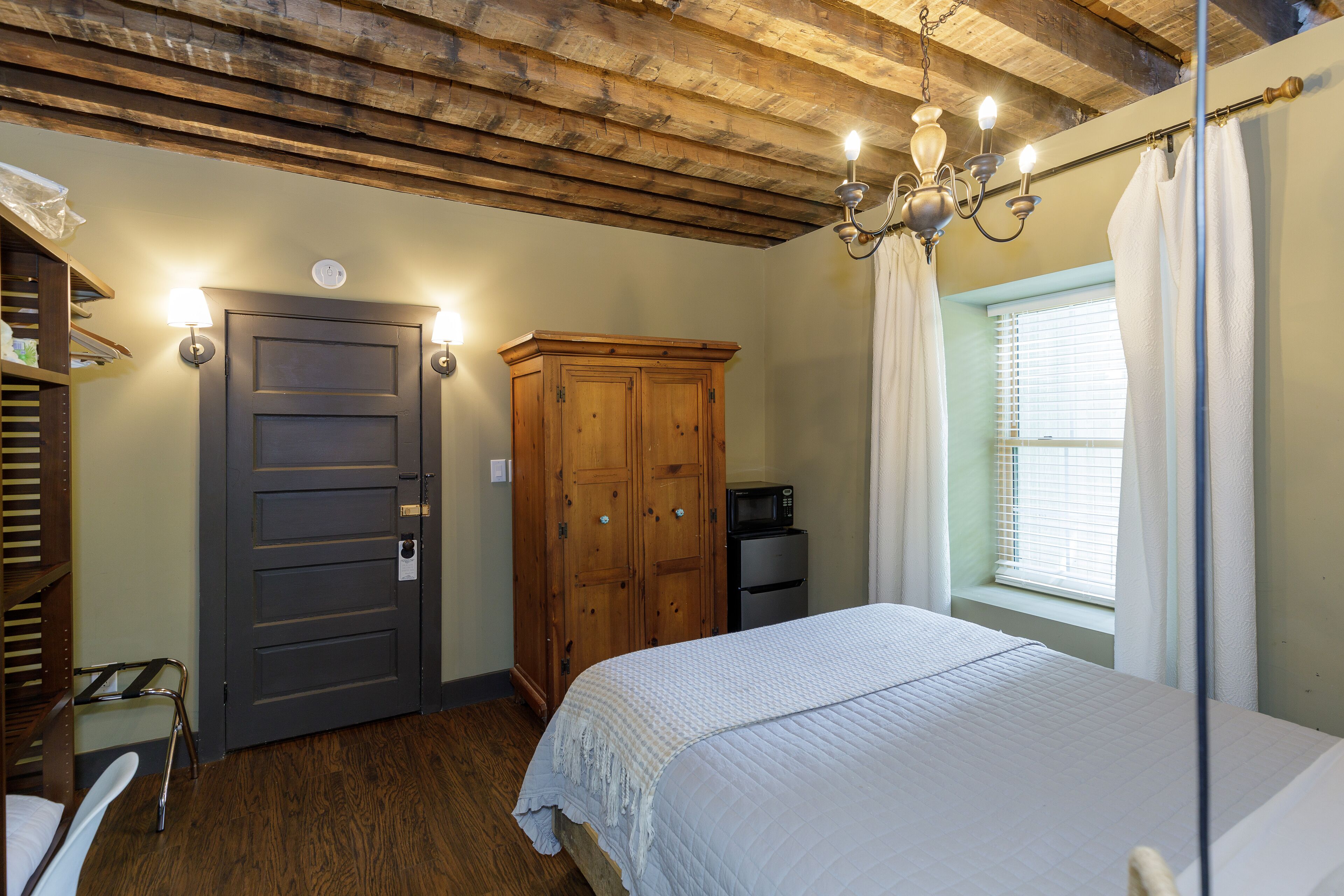 Un dormitorio con techo de madera, una cama, un armario, un escritorio y una ventana con cortinas.
