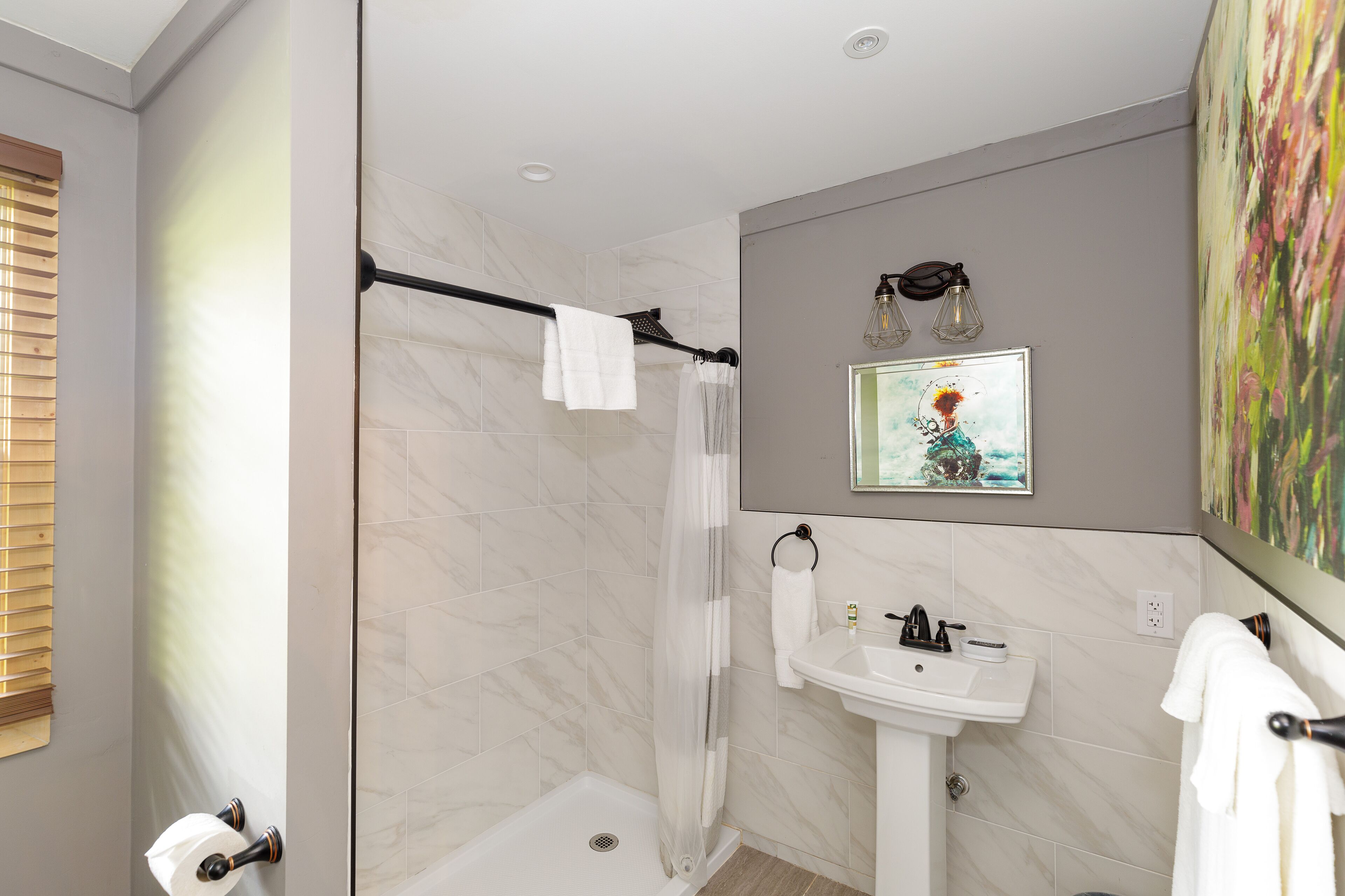 A modern bathroom with a shower, toilet, sink, and a painting on the wall.