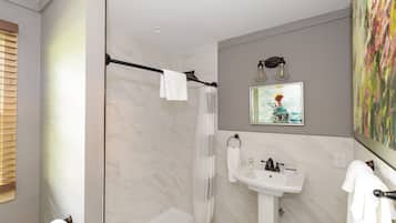 A modern bathroom with a shower, toilet, sink, and a painting on the wall.