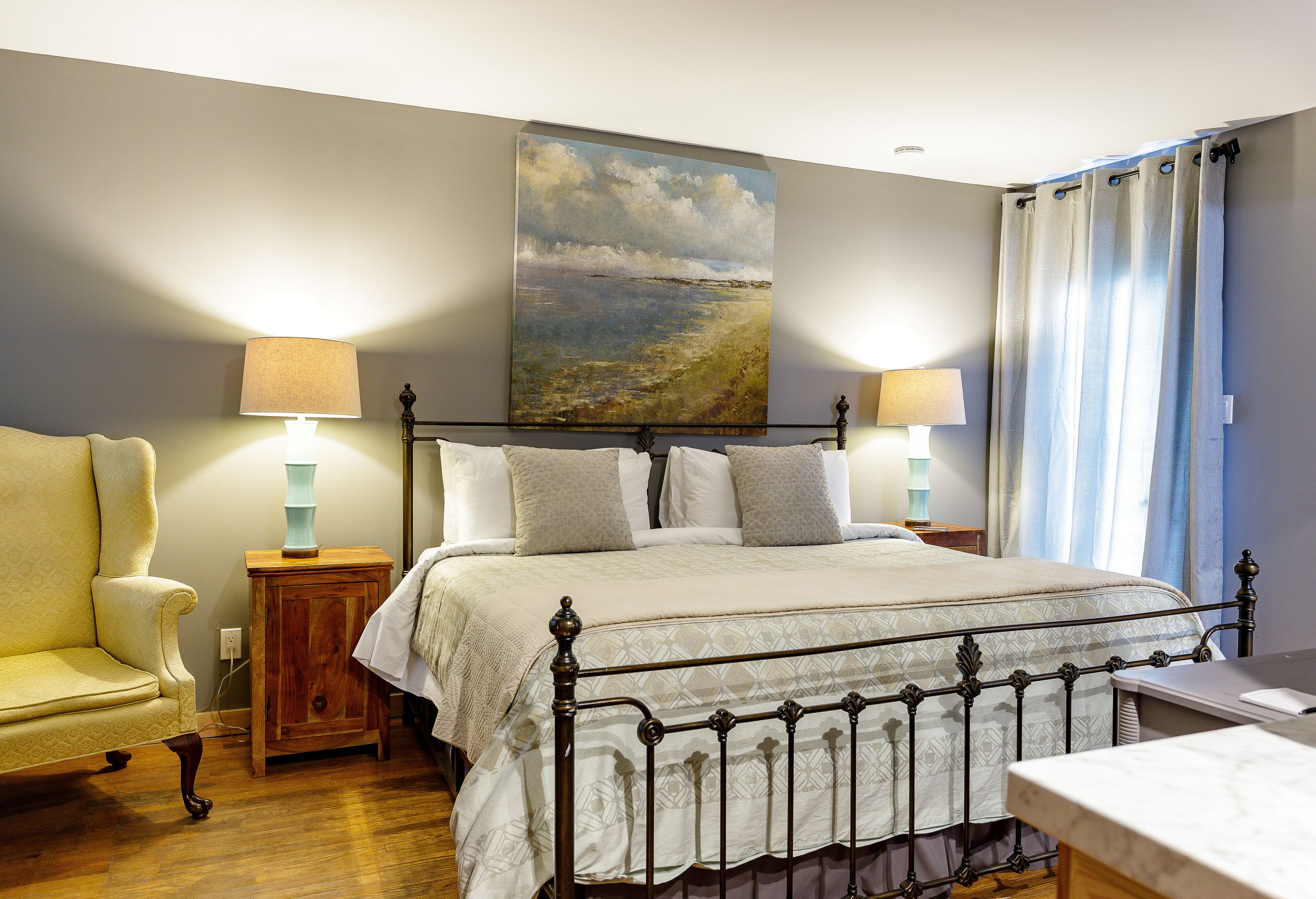 A bedroom with a bed, two bedside tables with lamps, a chair, and a painting on the wall.