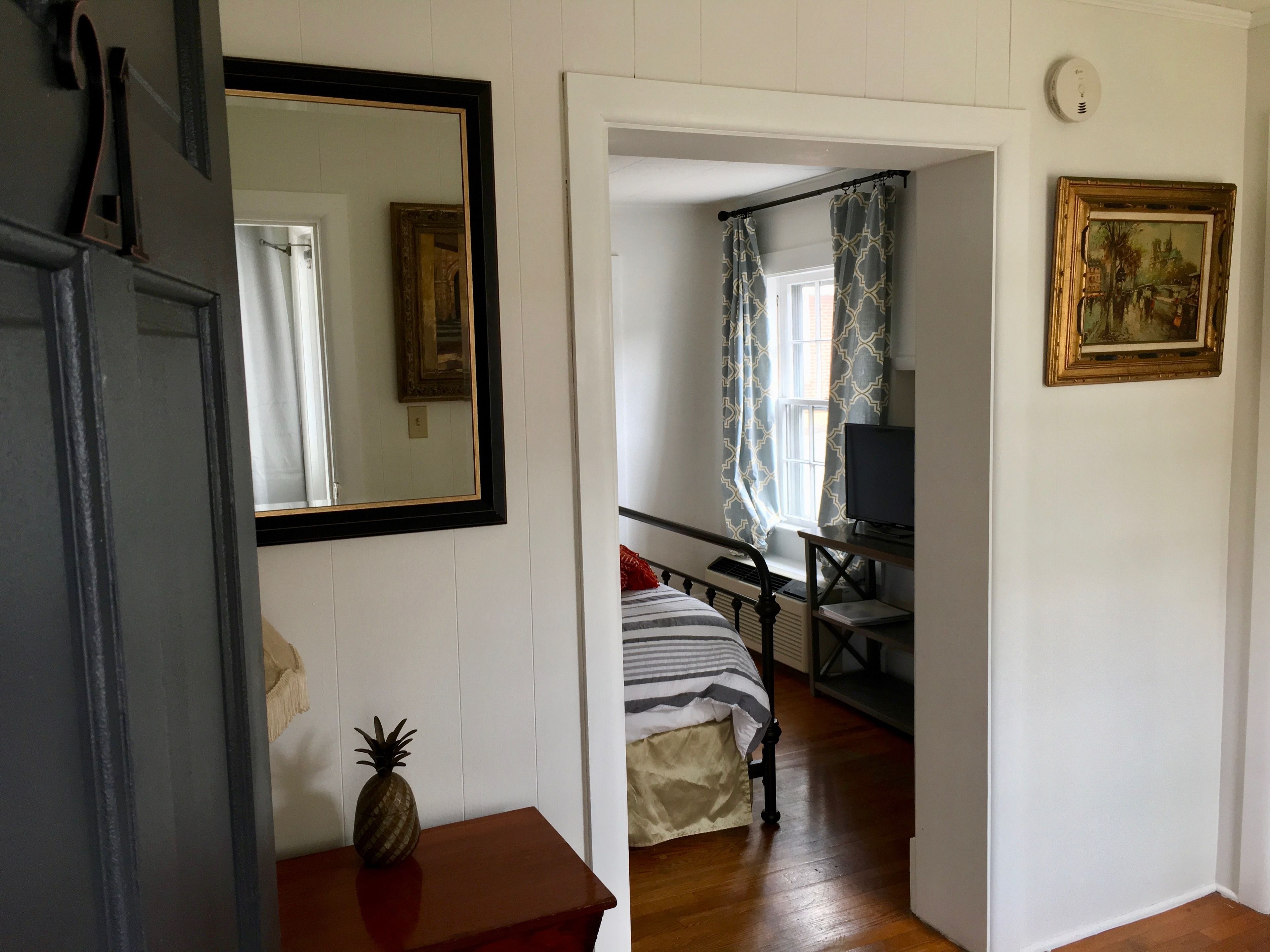 A room with a bed, a desk, a television, and a painting on the wall.