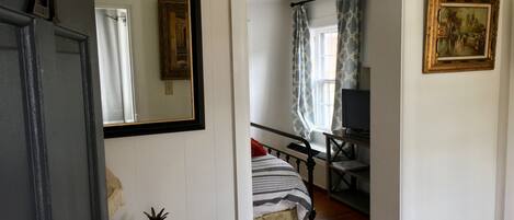 A room with a bed, a desk, a television, and a painting on the wall.