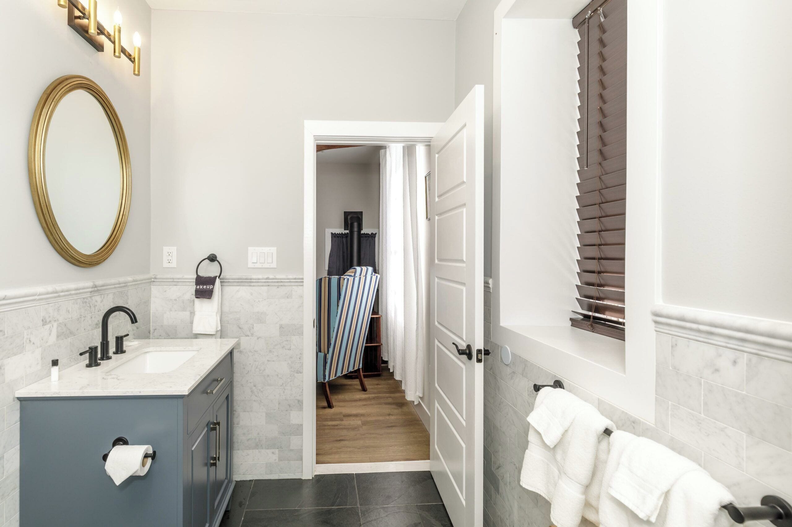 A bathroom with a sink, mirror, towel rack, and a door leading to another room.