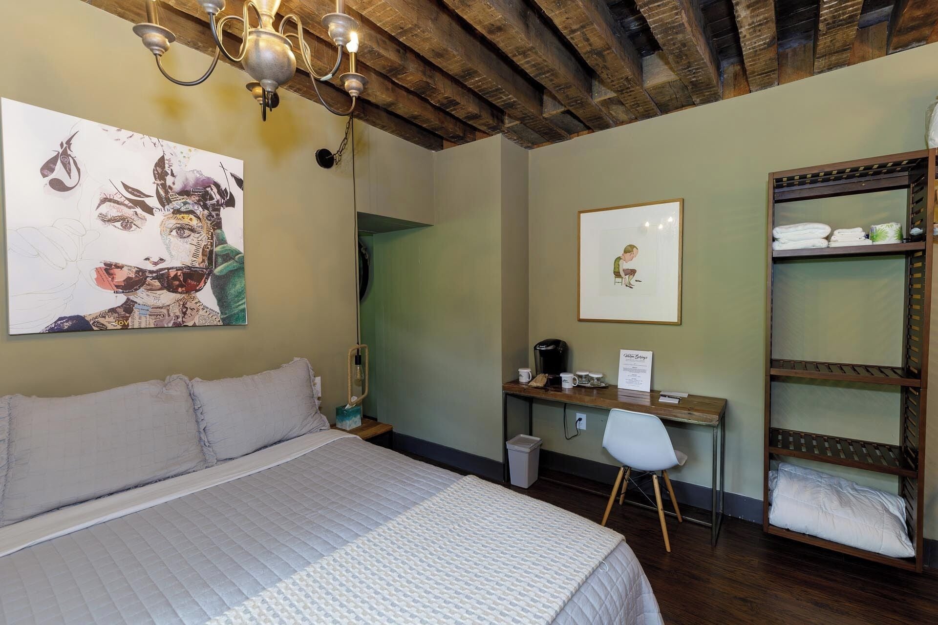 A bedroom with a bed, a desk, a chair, and a shelf with towels.