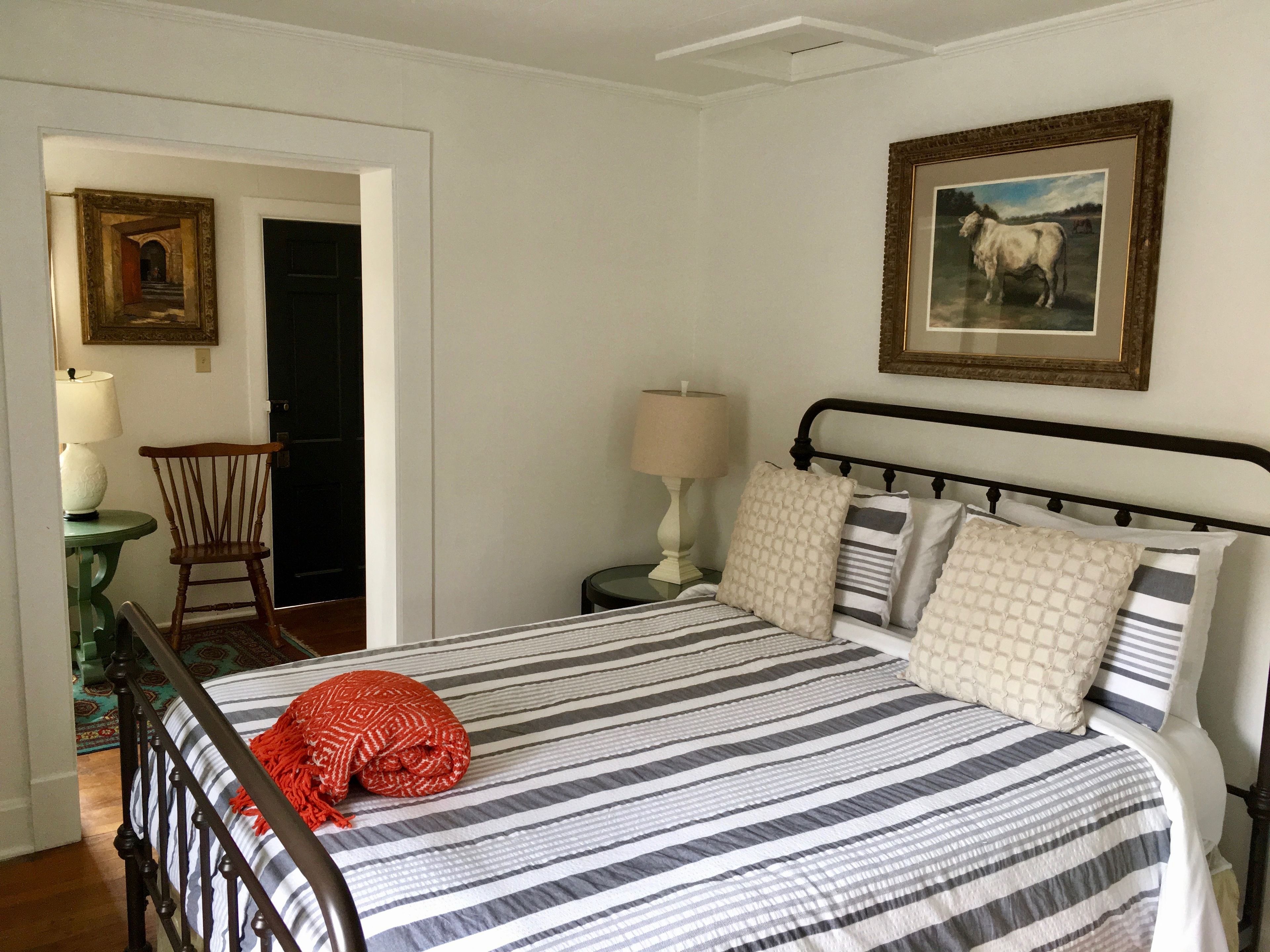 A bedroom with a bed, a chair, a nightstand, a lamp, and a framed picture on the wall.