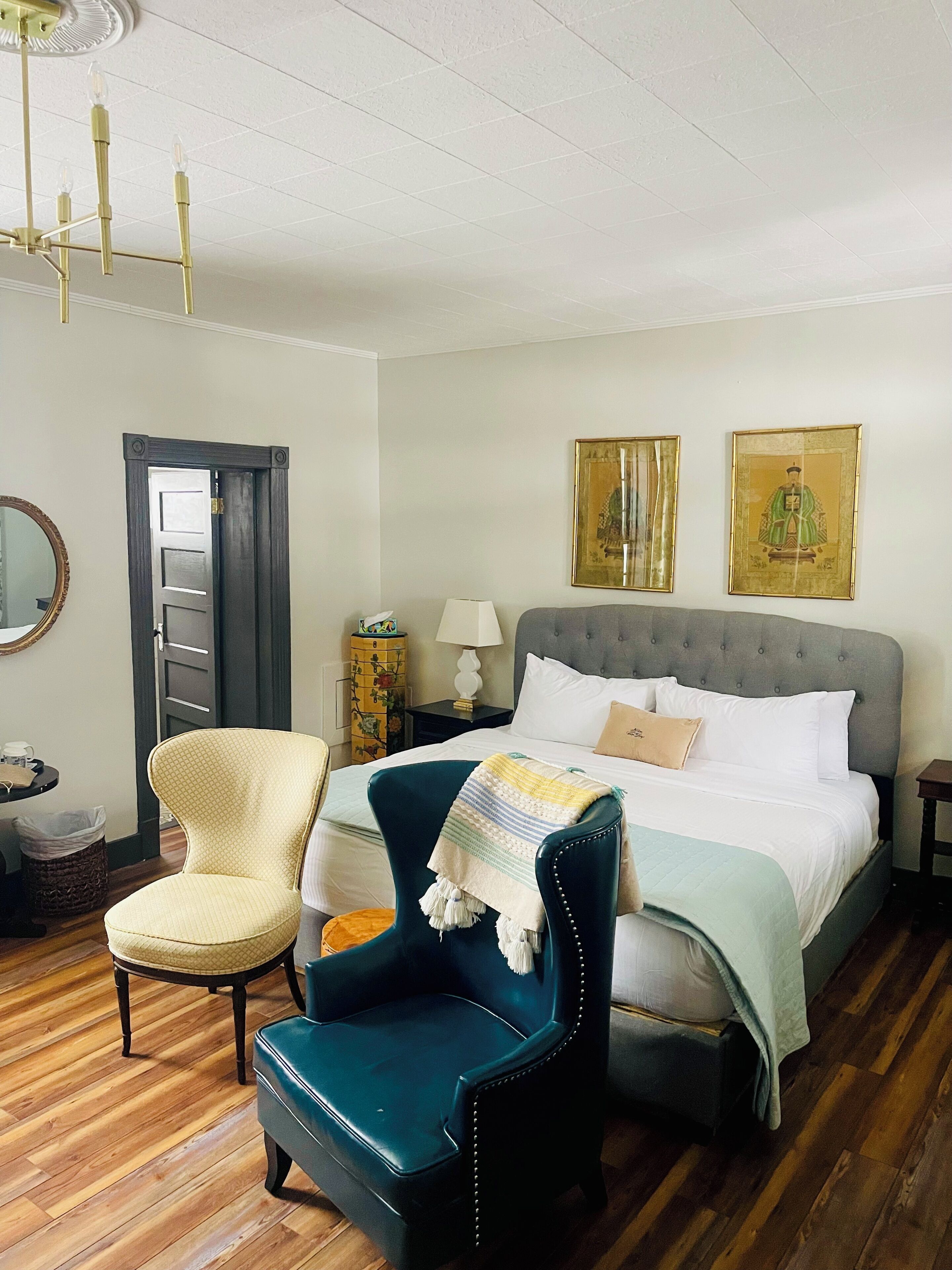 A bedroom with a bed, a chair, a nightstand, a lamp, and two framed pictures on the wall.