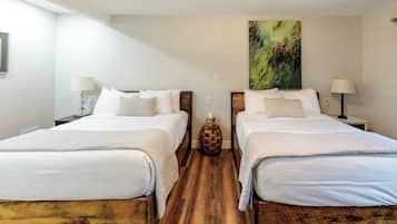 Habitación de hotel con dos camas, suelo de madera, ropa de cama blanca y un cuadro en la pared.