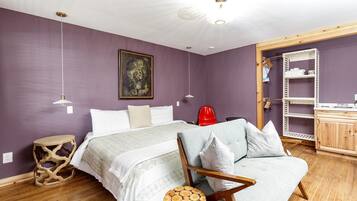 Un dormitorio con una cama, una silla, una mesita, un armario y un cuadro en la pared.