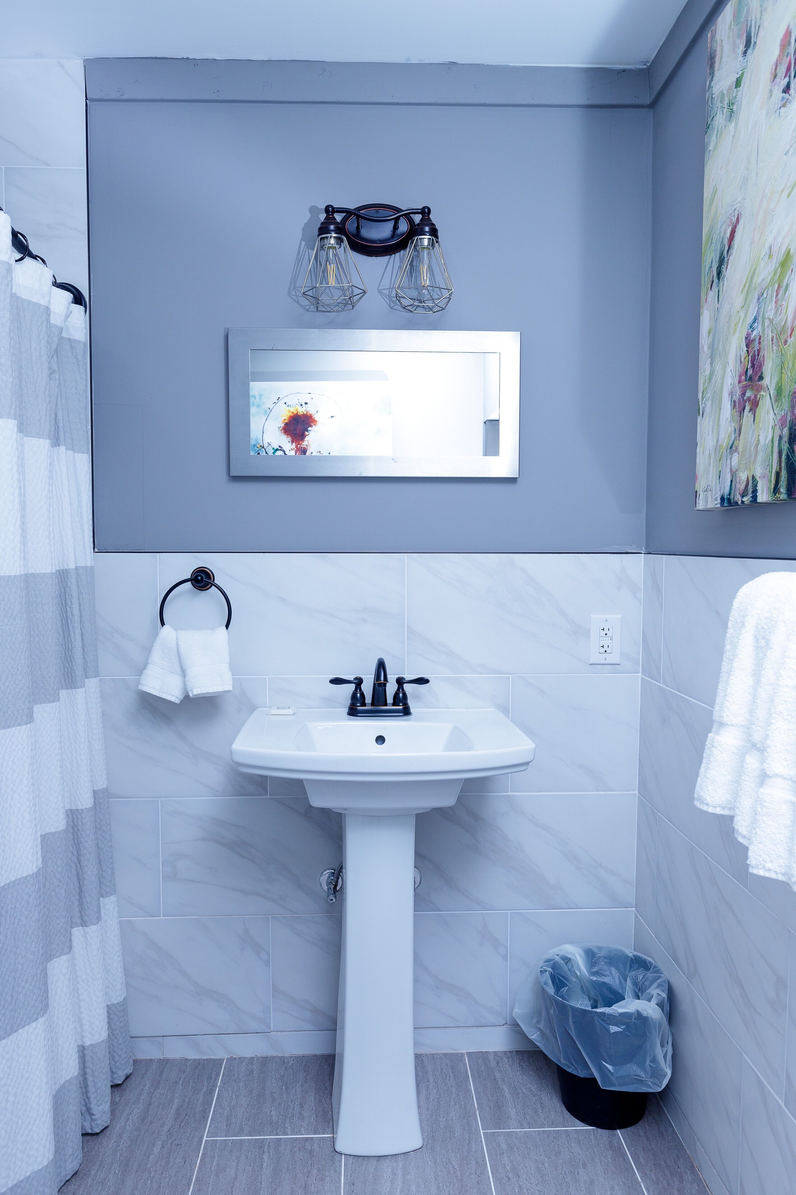 A bathroom with a white sink, a towel rack, a trash bin, and a shower curtain.