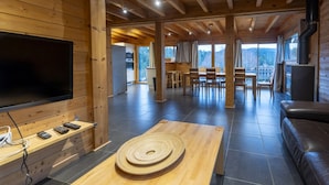 Interno moderno di una baita con zona pranzo in legno, un grande televisore e un camino.