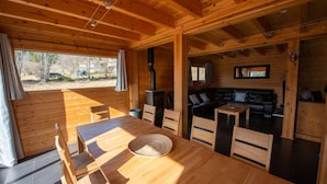 Interno di una baita in legno con zona pranzo, camino e soggiorno con divano e tavolino.