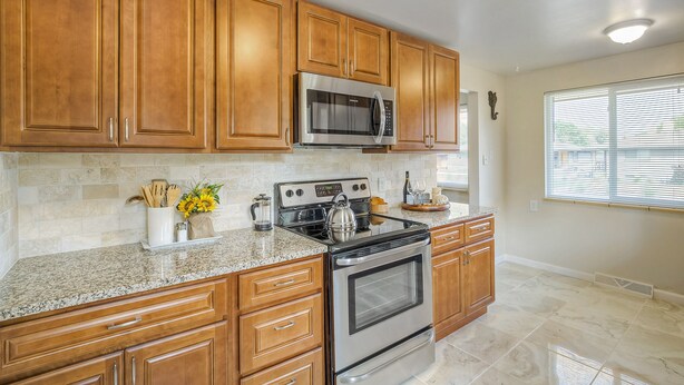 A kitchen with wooden cabinets, a stainless steel microwave, a gas stove, and granite countertops. - Convenient Access To Denver (Edgewater)