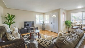 A living room with a leather sofa, a coffee table, and a TV. There is a door and a window in the background. - Convenient Access To Denver (Edgewater)