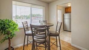 A dining area with a round table and four chairs, a potted plant, and a view through a window to the outside. - Convenient Access To Denver (Edgewater)