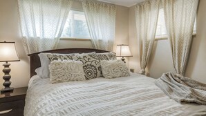A neatly made bed with a patterned bedspread, two bedside lamps, and a window with curtains. - Convenient Access To Denver (Edgewater)