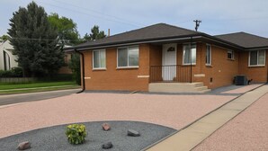 A two-story brick house with a front porch, a driveway, and a landscaped garden area with rocks and a small plant. - Convenient Access To Denver (Edgewater)