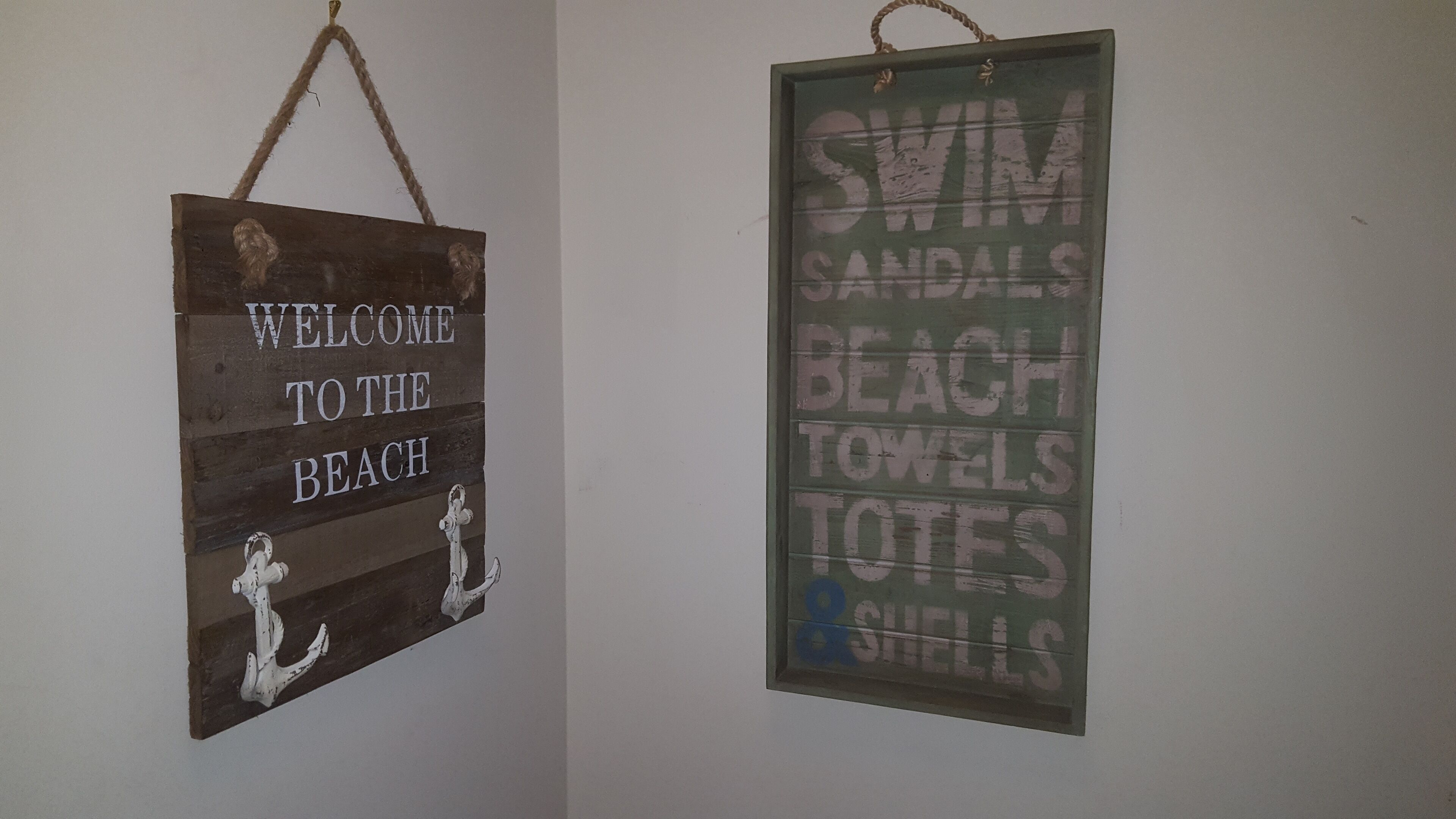 Two signs: one welcoming visitors to the beach and another listing beach-related items like swim sandals, towels, and shells.