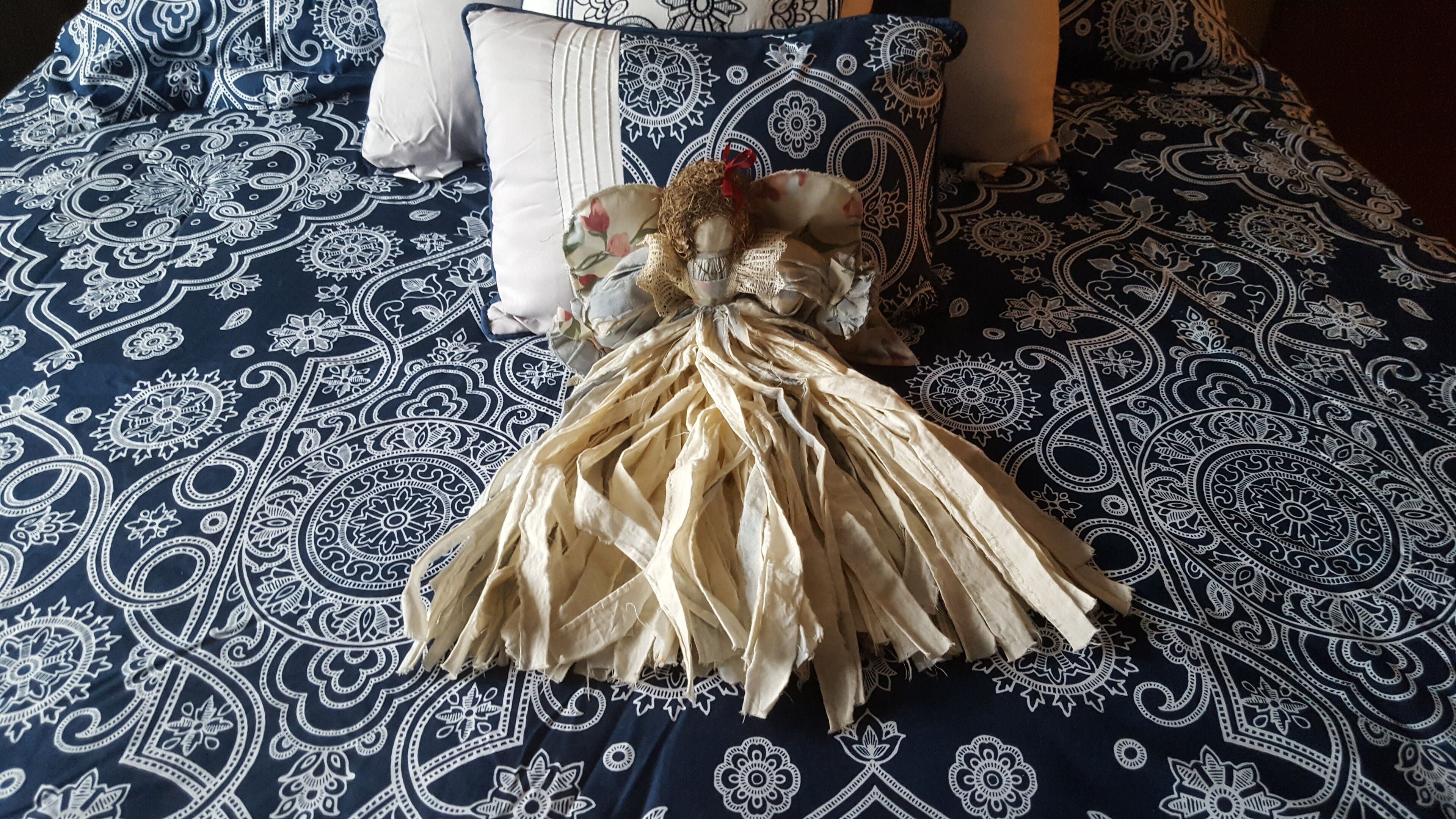 A bed with a blue and white patterned bedspread, a white pillow, and a decorative item resembling a dried plant or flower.