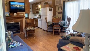 A cozy living room with a fireplace, a television, and a dining area with chairs and a table. - Beaver Lake Rent Cabin  Lg Covered Deck Room~Firepit~Quiet~Private~7Mi Rogers AR (Rogers)