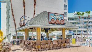 An outdoor bar area with tables and chairs, a sign for 'Cruzan Rum Suck', and a pool in the background.