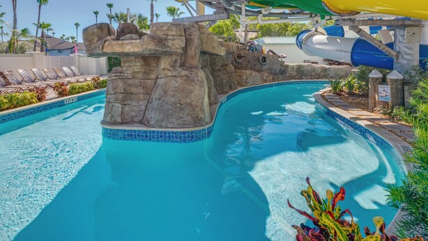 A pool with a water slide, lounge chairs, and a rocky wall.