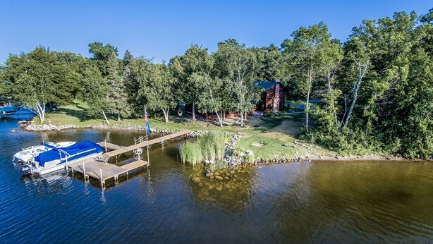 A lakeside property with a dock, boats, and a forested area.