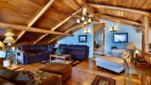 A spacious loft with a high wooden ceiling, a large leather sectional sofa, a white sofa, and a wooden coffee table.