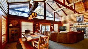 A log cabin interior with a dining area, a stone fireplace, and a cozy seating area.