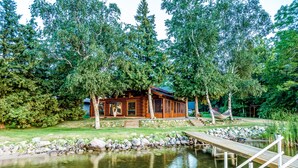 A wooden cabin with a dock extending into a pond, surrounded by dense trees.