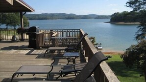 Een terras met buitenmeubilair met uitzicht op een meer, een barbecue en een overdekt gedeelte.