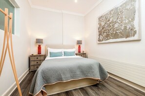 A bedroom with a bed, two bedside tables with lamps, a wooden easel, and a large floral painting on the wall.