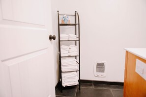 A bathroom with a towel rack holding neatly folded towels, a vent on the wall, and a white door.