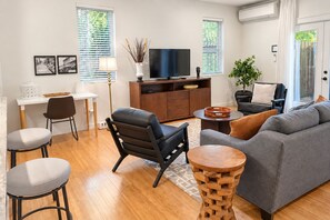 Una sala de estar moderna con un sofá, sillas, una mesa de centro, un televisor y un comedor con una mesa y sillas.